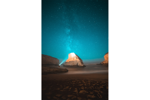 a man on a beach at night, illuminating a sea stack under the milky way, art, kanvas tablo